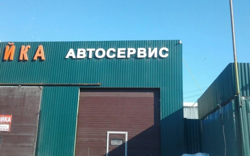 Белые несветовые буквы «Автосервис» над воротами на зелёном фасаде