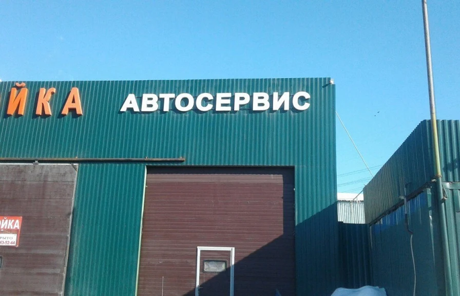 Белые несветовые буквы «Автосервис» над воротами на зелёном фасаде