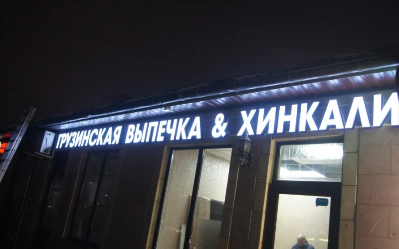 Светящаяся надпись «Грузинская выпечка & хинкали» над окнами, вид снизу