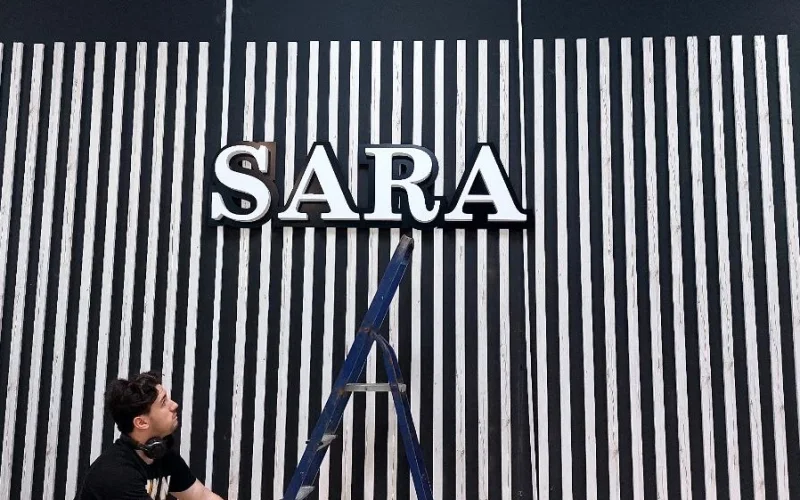 Несветовая вывеска SARA с белыми буквами над входом в магазин Несветовая вывеска SARA с белыми буквами над входом в магазин