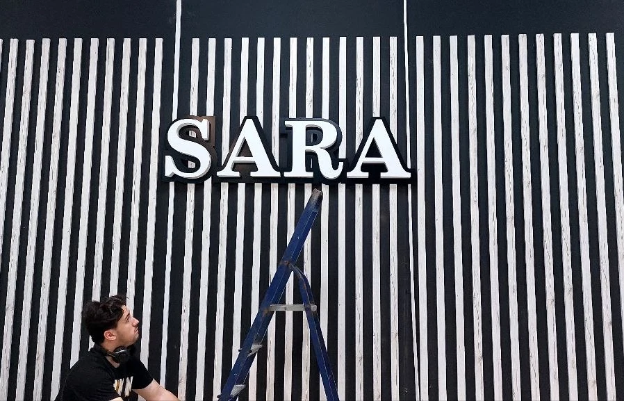 Несветовая вывеска SARA с белыми буквами над входом в магазин