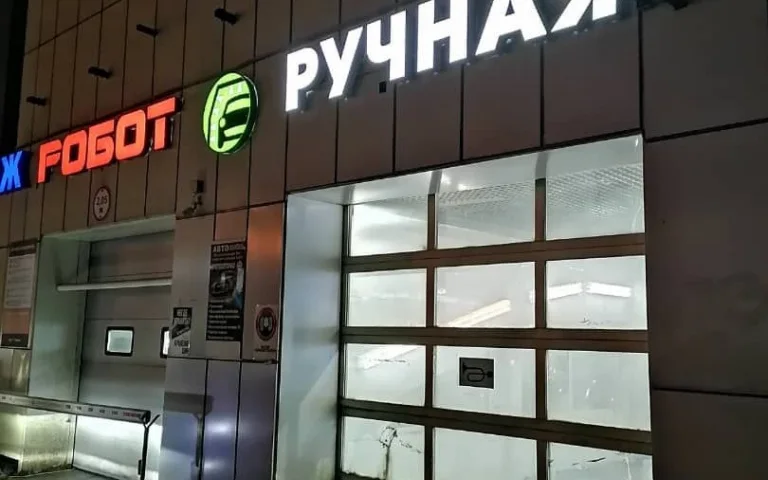 Белые световые буквы «Ручная» на фасаде автомойки рядом с соседними обозначениями