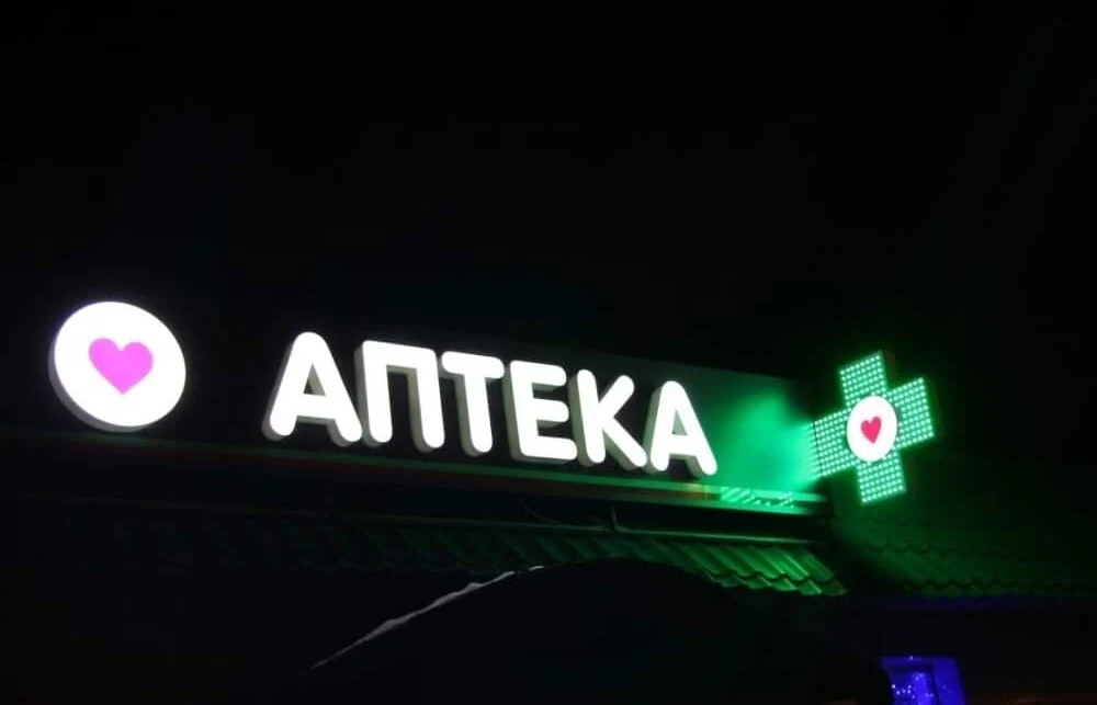 Вывеска «АПТЕКА» и зелёный пиксельный аптечный крест на фасаде ночью