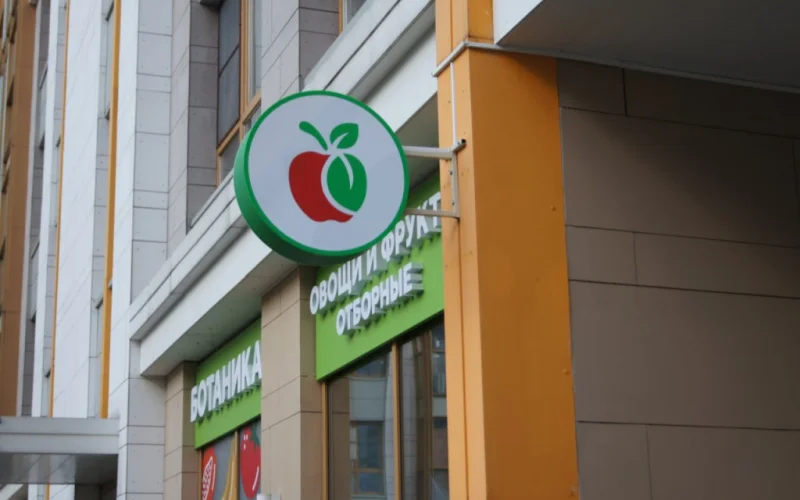 Круглый панель-кронштейн с красно-зелёным яблоком на фасаде магазина