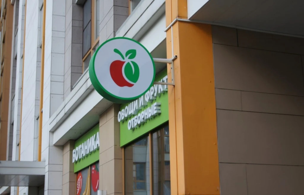 Круглый панель-кронштейн с красно-зелёным яблоком на фасаде магазина