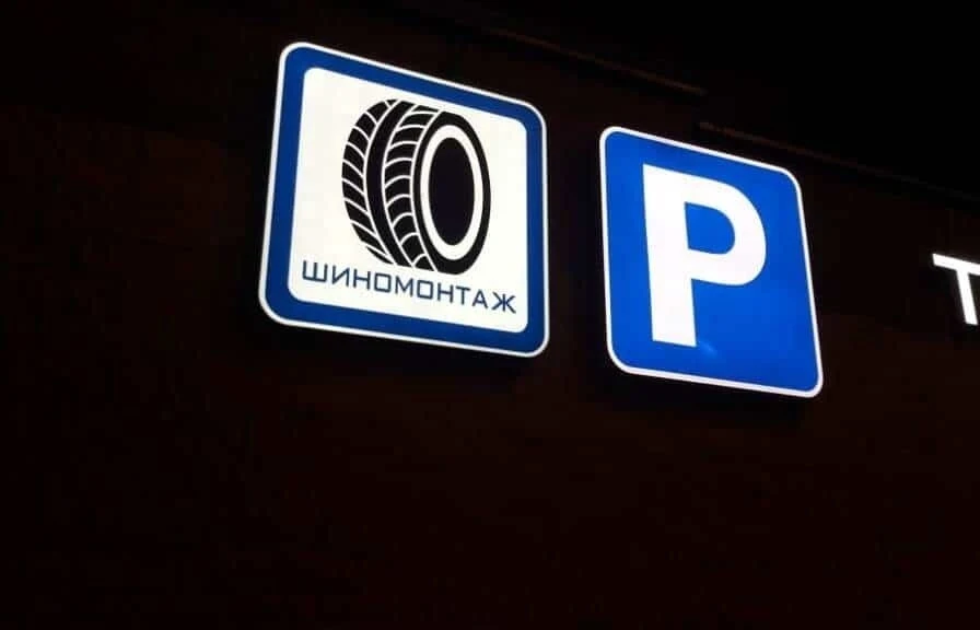 Установленный световой короб «Шиномонтаж» рядом с обозначением парковки вечером