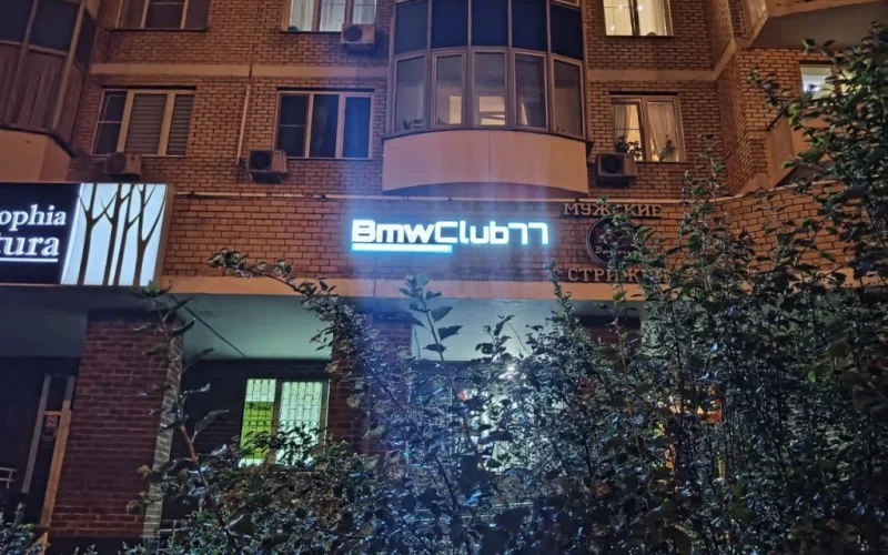 Световая вывеска BMW Club 77 на кирпичном фасаде вечером