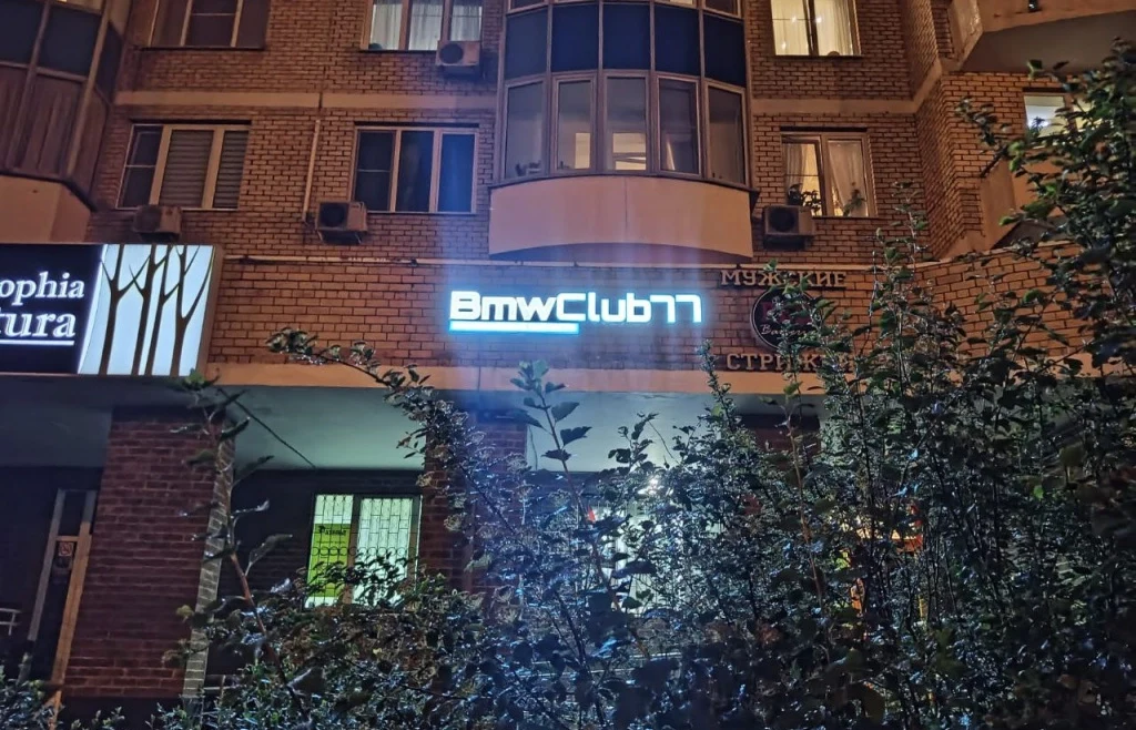 Световая вывеска BMW Club 77 на кирпичном фасаде вечером