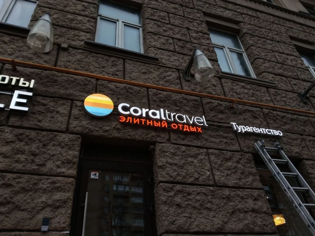 Световая вывеска Coral Travel с оранжевой строкой «Элитный отдых» на фактурном фасаде