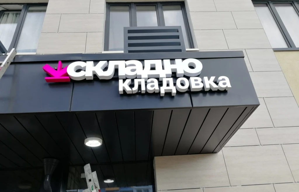 Белые объёмные буквы «Складно кладовка» и розовый знак на тёмном козырьке