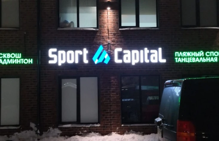 Белые световые буквы Sport Capital с голубым геометрическим логотипом