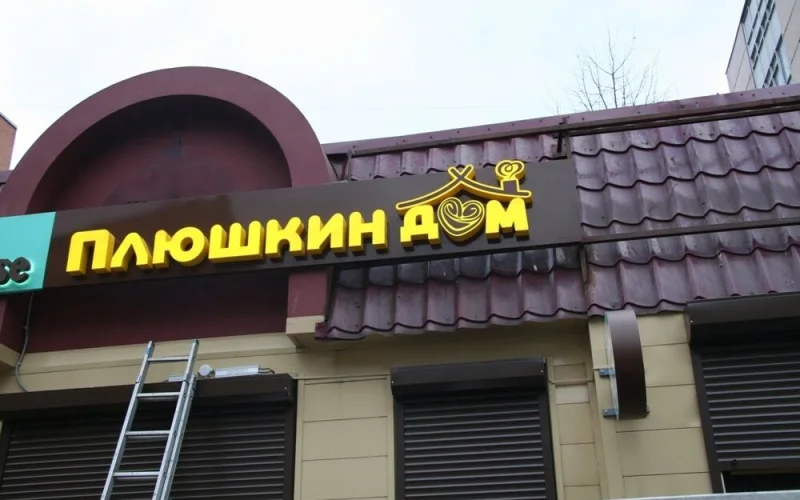 Жёлтые световые буквы «Плюшкин дом» на тёмной подложке