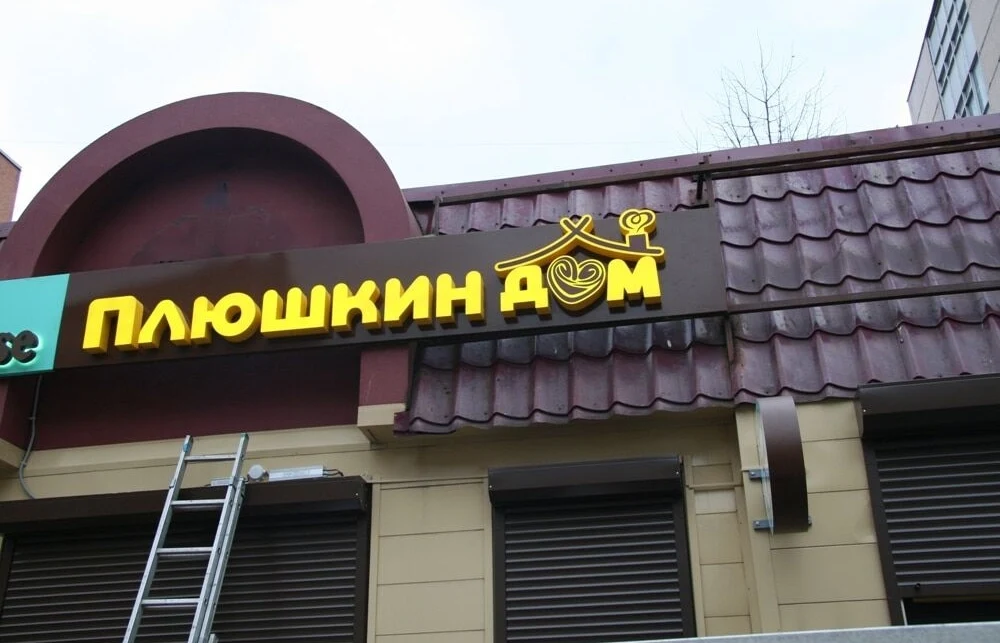 Жёлтые световые буквы «Плюшкин дом» на тёмной подложке