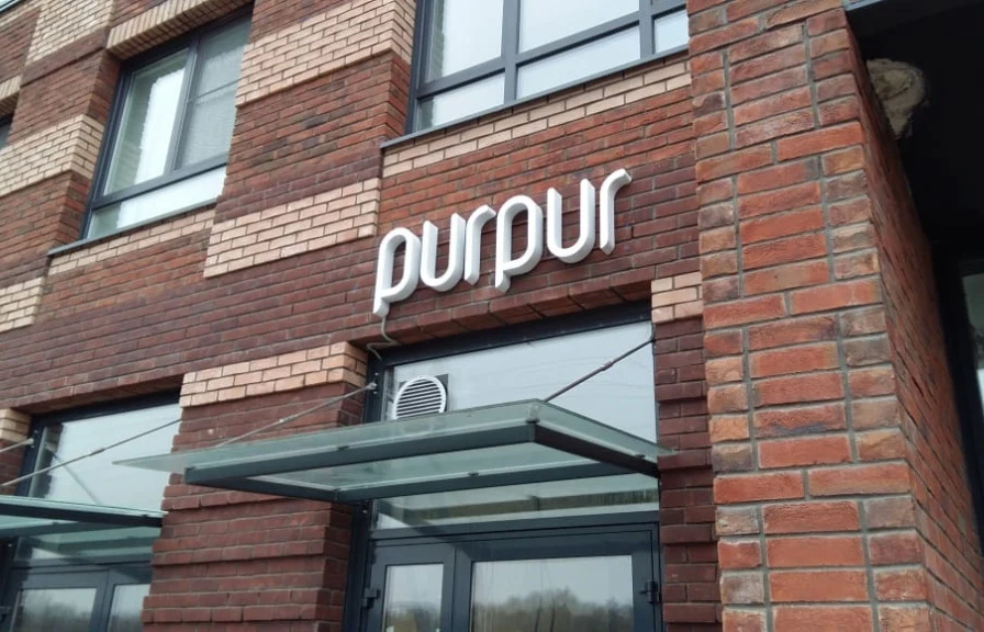 Световая вывеска PurPur на кирпичном фасаде над входом