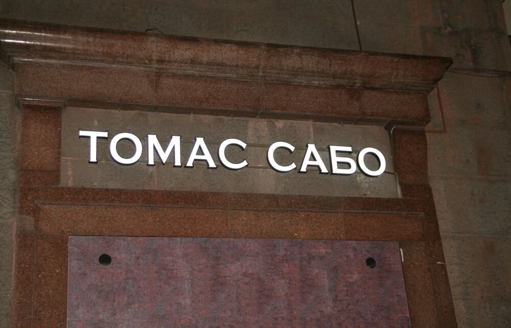 Белые световые буквы «ТОМАС САБО» внутри архитектурного обрамления фасада