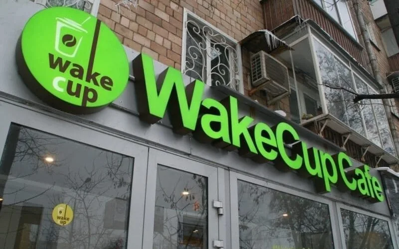 Зелёные объёмные буквы Wake Cup Cafe и круглый логотип днём